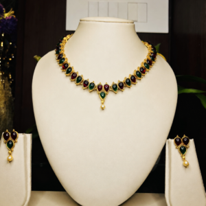 Antique gold-toned traditional necklace and earring set with alternating maroon and green kemp stones in teardrop shapes, finished with a pearl drop pendant, displayed on an off-white velvet bust – South Indian Kemp temple jewellery by Santosree Collective
