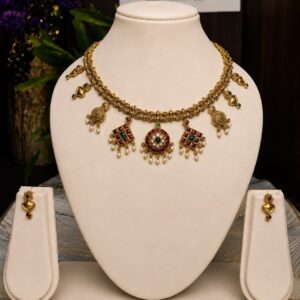 Antique gold Kemp temple jewellery necklace set with matching earrings – round kundan pendant with red, green and pearl detailing, diamond-shaped kemp motifs, pearl drops, and peacock accents, displayed on cream velvet bust