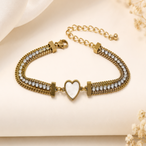 Gold-toned layered chain bracelet with crystal-studded double chain design and mother-of-pearl heart charm centerpiece, laid flat on a cream background with dried flowers – anti-tarnish daily wear jewellery by Santosree Collective