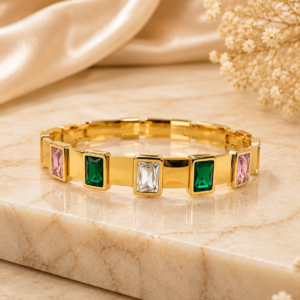 Gold-toned bangle bracelet with multicolor baguette-cut crystals in pink, green, and clear stones, displayed on cream satin with dried flowers – anti-tarnish daily wear jewellery by Santosree Collective