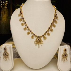 Antique gold-toned traditional necklace and earring set with sunflower-style floral motifs, maroon kemp stones, and pearl drop accents, displayed on an off-white velvet bust – South Indian Kemp-style temple jewellery by Santosree Collective