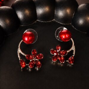 A pair of red floral Korean-style earrings with glossy red pearl studs and sparkling red flower drops, displayed on a black textured tray with red dried flowers in the background