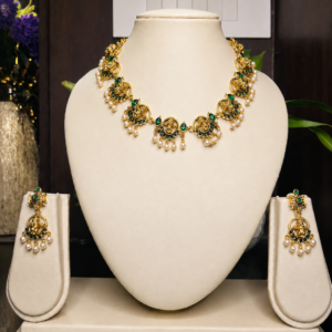 Antique gold-toned temple necklace and earring set with repeating deity motif medallions, green stone accents, and pearl drop detailing, displayed on an off-white velvet bust – South Indian temple jewellery by Santosree Collective
