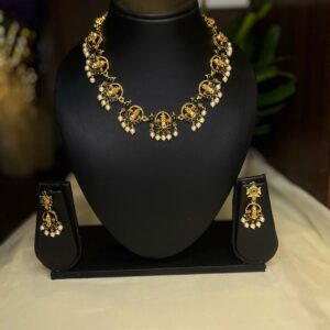 Vishnu Tilaka Traditional Necklace Set displayed on a black jewellery bust with matching earrings on both sides. The set has an antique gold finish, green stone detailing and pearl drop accents, styled on a soft cream fabric background with warm lighting.